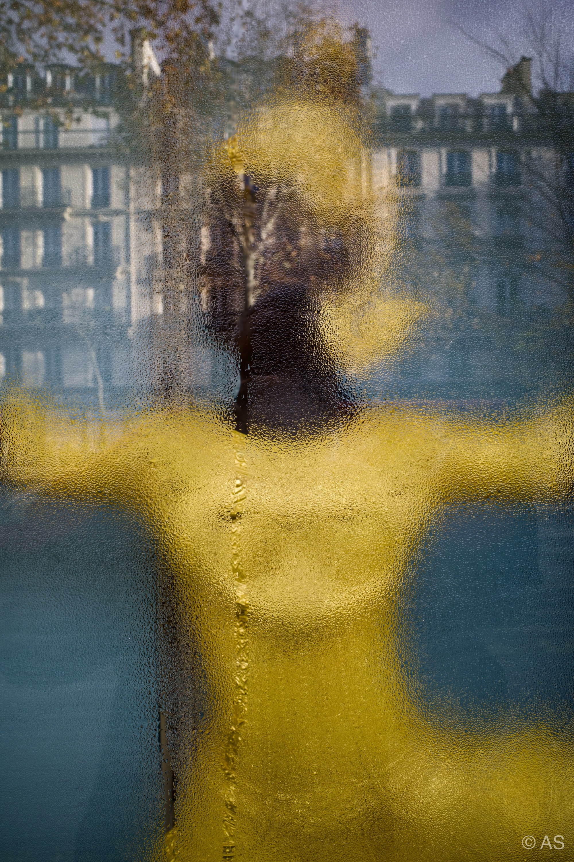 Golden mannequin seen through frosted wet glass with Parisian buildings reflected